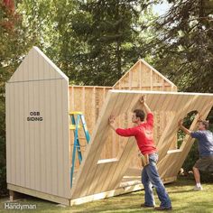 two men are building a shed in the yard with their hands up and one man is standing next to it