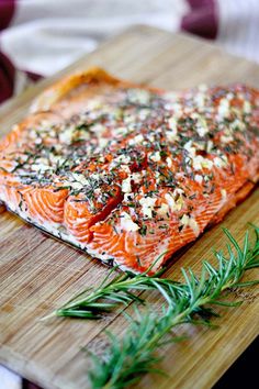 a piece of salmon on a wooden cutting board with herbs and seasoning sprinkles