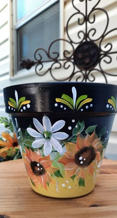 a painted flower pot sitting on top of a wooden table next to a metal planter