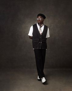 a man standing in front of a dark background wearing a black vest and white shirt