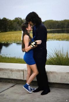 a man in a suit and tie kissing a woman on the cheek while standing next to a lake