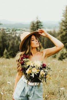 a woman with a hat and flowers on her head is standing in the middle of a field