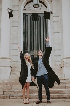 a man and woman standing in front of a building holding their hands up to the sky