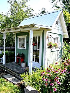 a small green and white shed sitting in the middle of a lush green field with flowers