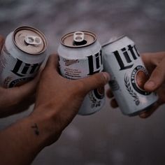 two cans of beer being held by someone's hands in front of the camera