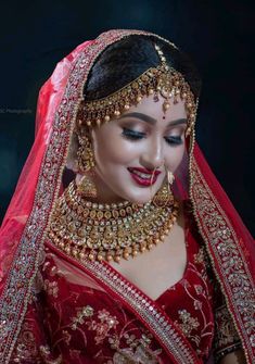 a woman wearing a red and gold bridal outfit with jewelry on her neck, in front of a black background