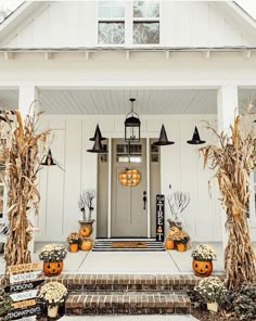 a white house decorated for halloween with pumpkins and corn stalks on the front porch