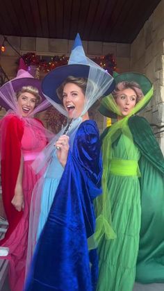 three women dressed in costume posing for the camera with hats on their heads and gowns draped around them