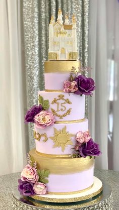 a three tiered cake with purple flowers and gold trimmings on a table