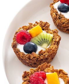 some fruit and yogurt cups are on a white plate with strawberries, kiwis, raspberries, and blueberries