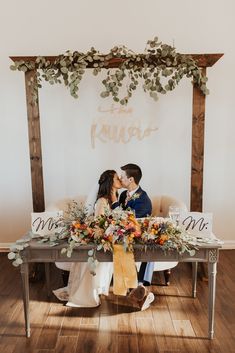 a bride and groom sitting on a bench with their wedding signs in front of them