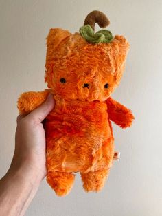 a hand holding an orange teddy bear with a green leaf on it's head