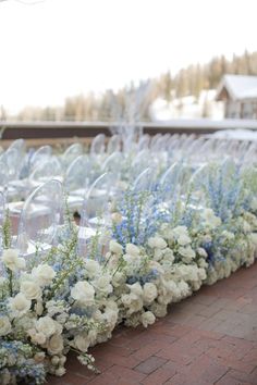 a row of clear vases filled with white and blue flowers on top of a brick walkway