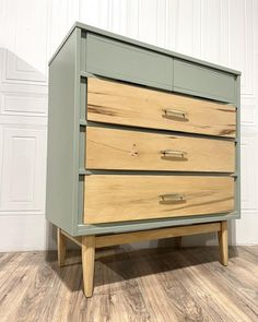 a green dresser with three drawers on top of wooden flooring and white walls in the background