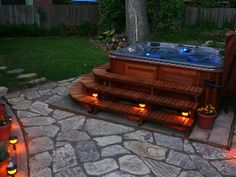 a hot tub in the middle of a patio with lights on it and steps leading up to it