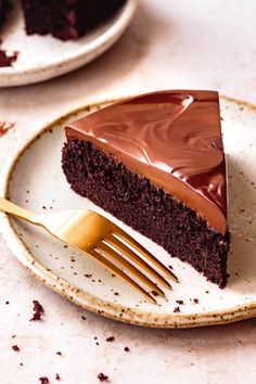 a slice of chocolate cake on a white plate with a gold fork next to it