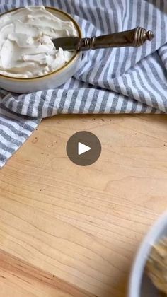 a bowl of whipped cream next to a wooden cutting board with a spoon on it