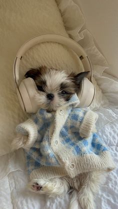 a small dog wearing headphones laying on top of a white bed covered in blankets