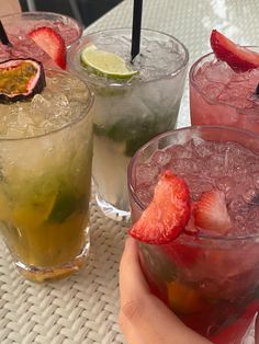 three glasses filled with different types of drinks on top of a white table next to strawberries and limes