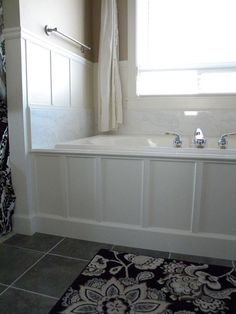 a bath tub sitting under a window next to a rug