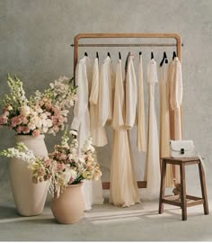 an arrangement of wedding gowns and flowers in vases next to a dress rack