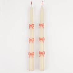 two white candles with pink bows on them sitting side by side against a white background