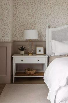 a white bed sitting next to a nightstand with a lamp on top of it in a bedroom