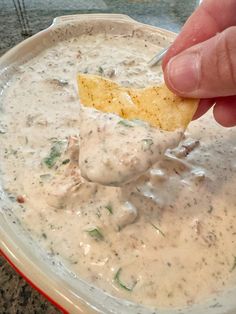 a hand dipping a tortilla chip into a bowl of dip