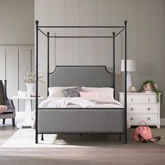 a bedroom with a four poster bed, dresser and chair next to it in front of a white wall