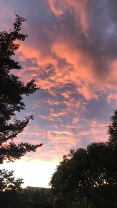 the sun is setting behind some trees and clouds in the sky, with no one visible