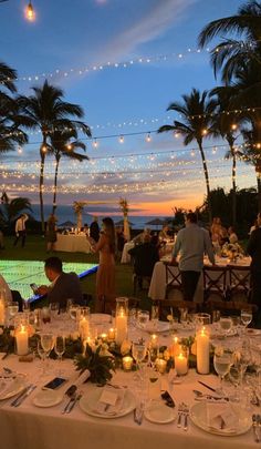 people are sitting at tables in front of palm trees with lit candles on the table