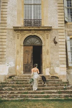 a woman in a wedding dress walking up the steps to a building with a dog