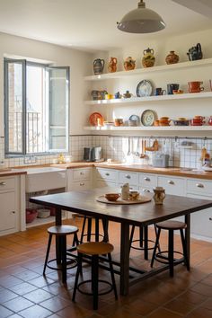 This kitchen brings warmth with its terracotta floor tiles and open shelving adorned with colorful Spanish ceramics.

The natural wood countertop adds a grounded element, while the farmhouse sink provides a rustic yet functional touch.

Sunlight streams through the window, enhancing the earthy ambiance.