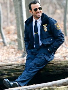 a man in a police uniform is sitting on a fallen tree trunk and smiling at the camera