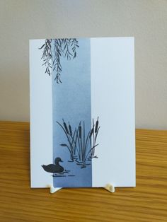 a card with an image of a duck and reeds on the water's edge