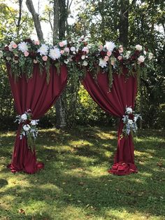 two red drapes with white flowers and greenery on them in front of trees