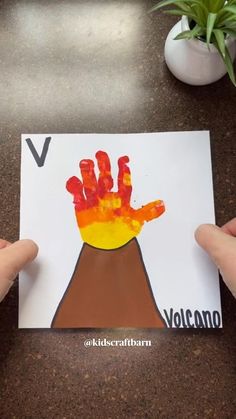 two hands holding up a handprint with the letter v on it and an volcano in the background