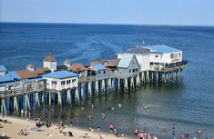 people are on the beach and in the water near a pier that is built into the ocean