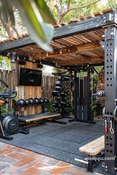 an outdoor gym area with equipment and trees in the background, including a bench, treadmills, and television