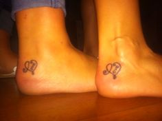 two people with tattoos on their feet sitting next to each other at a wooden table