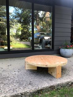 a wooden table sitting in front of a window on the side of a house next to a potted plant