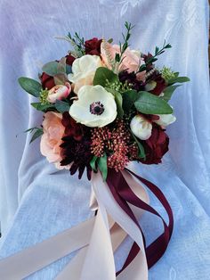 a bridal bouquet with roses and greenery on a white cloth draped over it