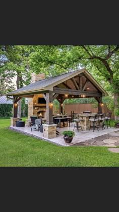 a covered patio with an outdoor kitchen and grill in the back yard, surrounded by trees