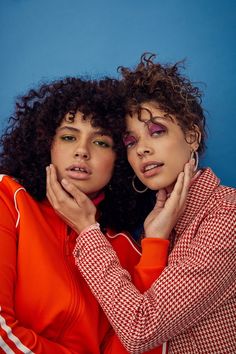 two women are posing for the camera with their hands on their chins and one is wearing an orange top