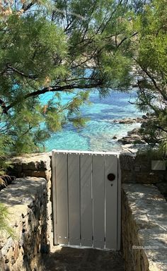 an open gate on the side of a stone wall next to some trees and water