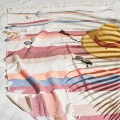 a hat and sunglasses are laying on a striped blanket with other items scattered about it