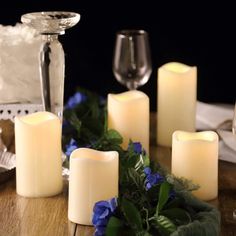 lit candles on a wooden table with blue flowers and greenery around it, next to wine glasses