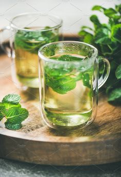 two glasses of green tea on a wooden tray with mint leaves in the foreground