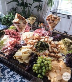 an assortment of cheeses, meats and grapes on a tray with wine glasses