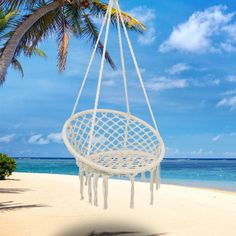 a white hanging chair on the beach with palm trees